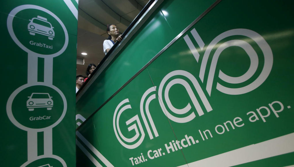 Commuters pass Grab transport booking service app advertisements at a train station in Singapore